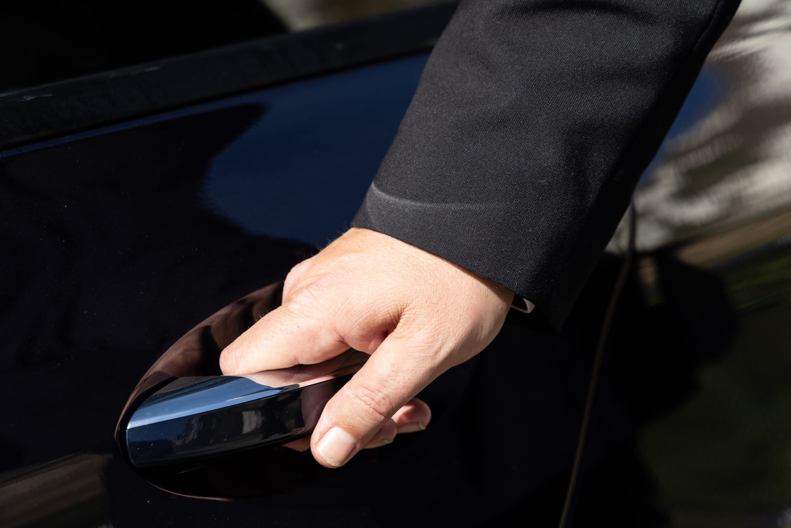 A chauffeur's hand on a car door handle